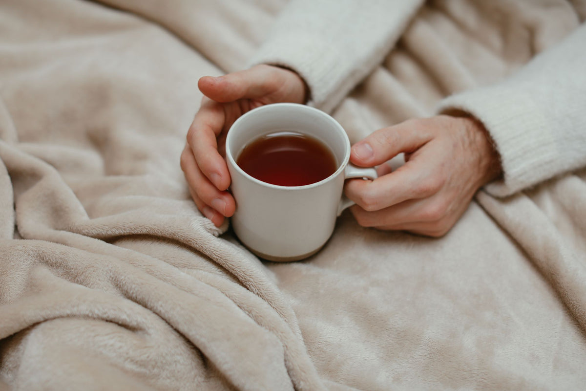 Mains autour d'une tasse de thé sous un plaid beige